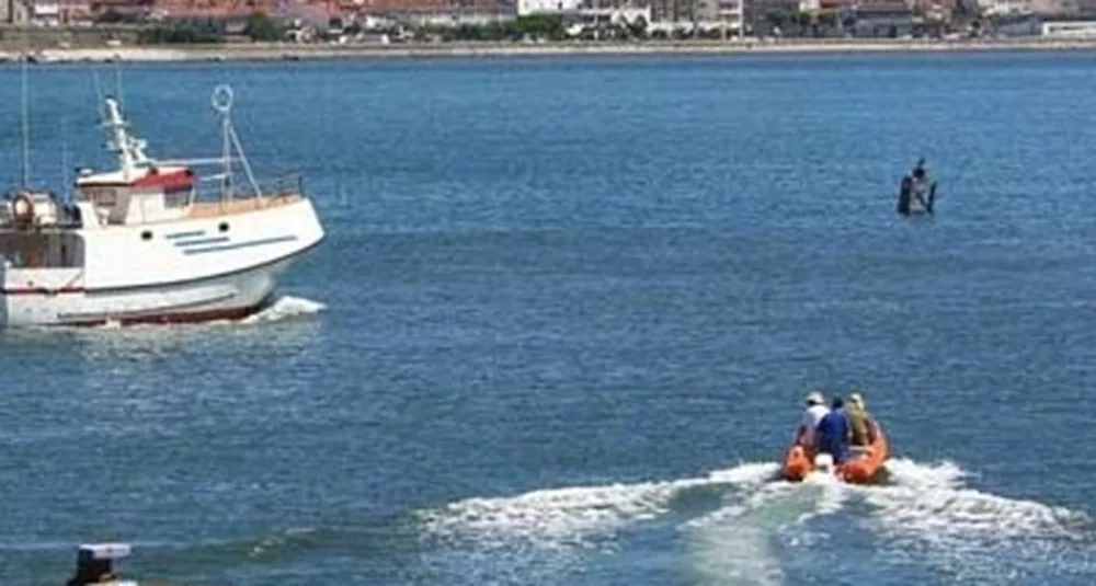 Barco de pesca e um bote insuflável de resgate no mar, junto à costa