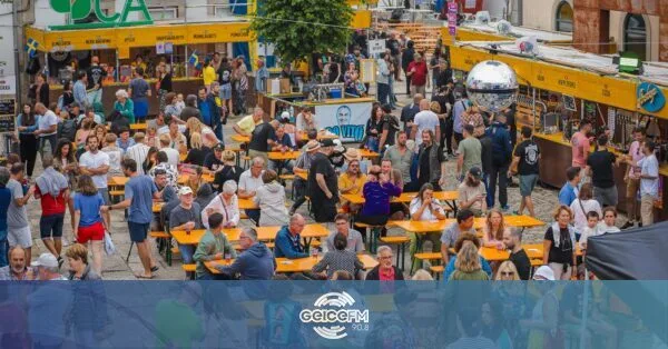 Multidão num festival de cerveja ao ar livre, com mesas e tendas junto a edifícios antigos