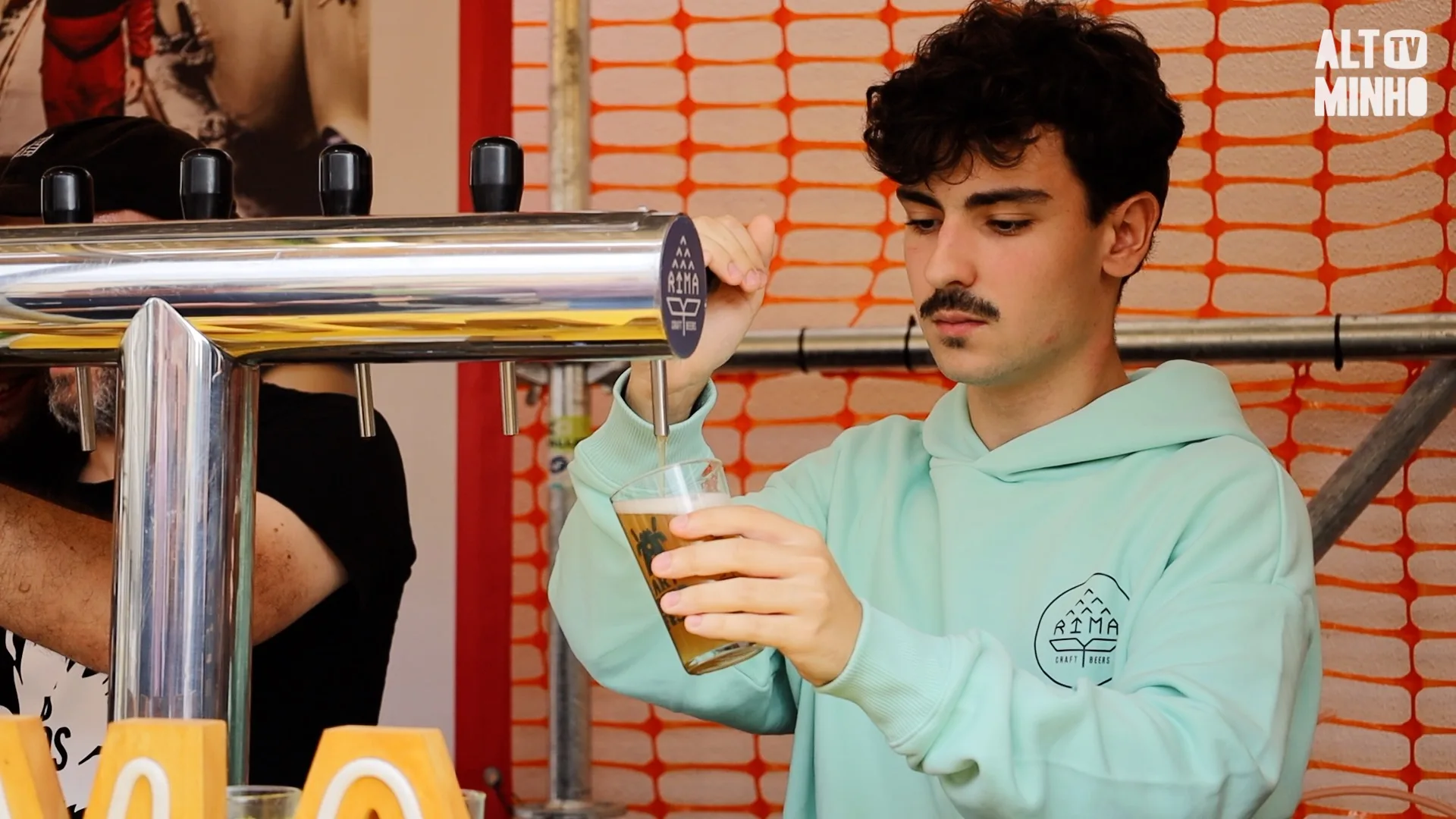Jovem enche um copo de cerveja artesanal numa torneira, com logótipo Rima Craft Beers na camisola